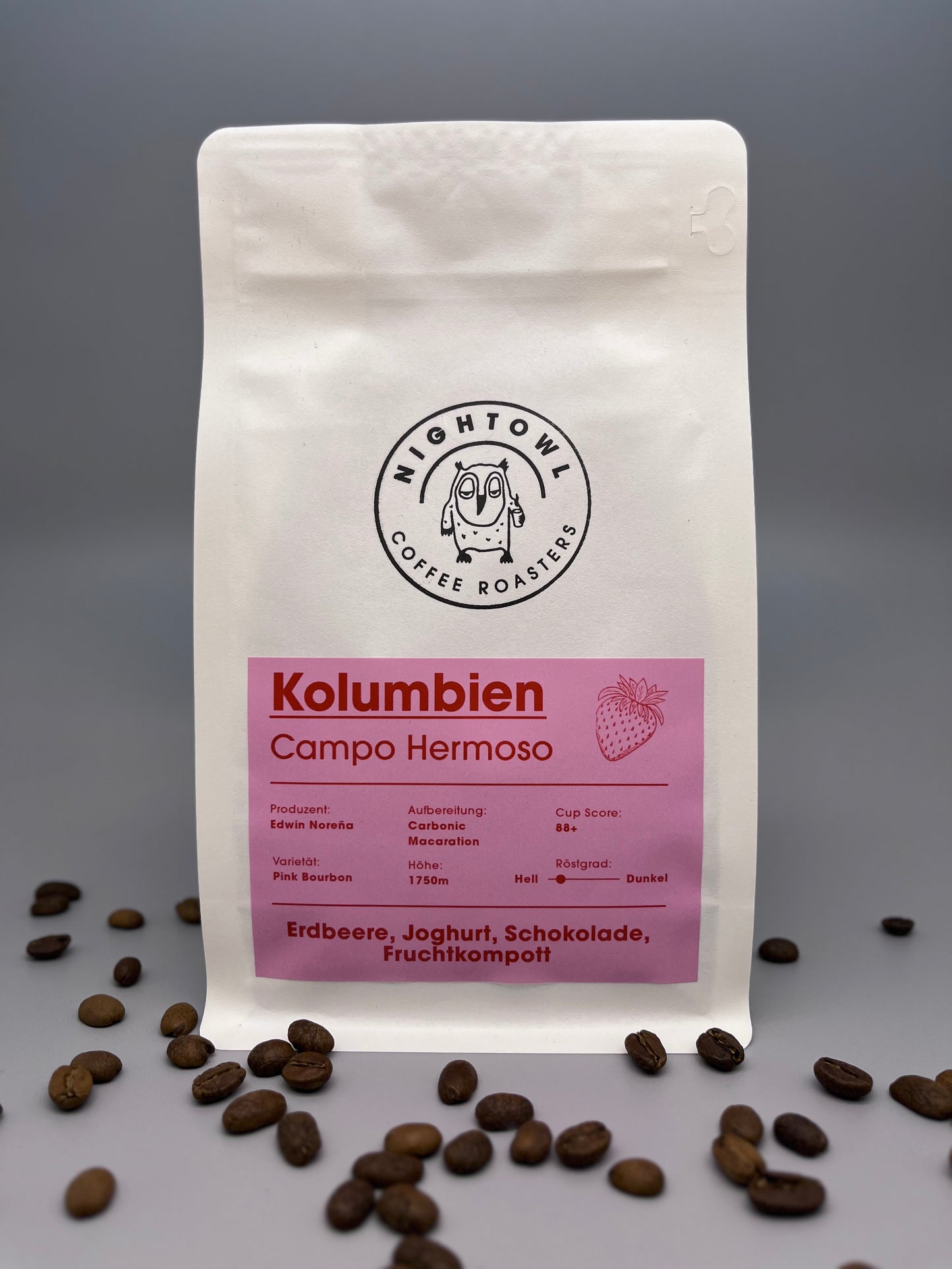 Kaffeeverpackung mit rosa Etikett, Bohnen liegen im Vordergrund.