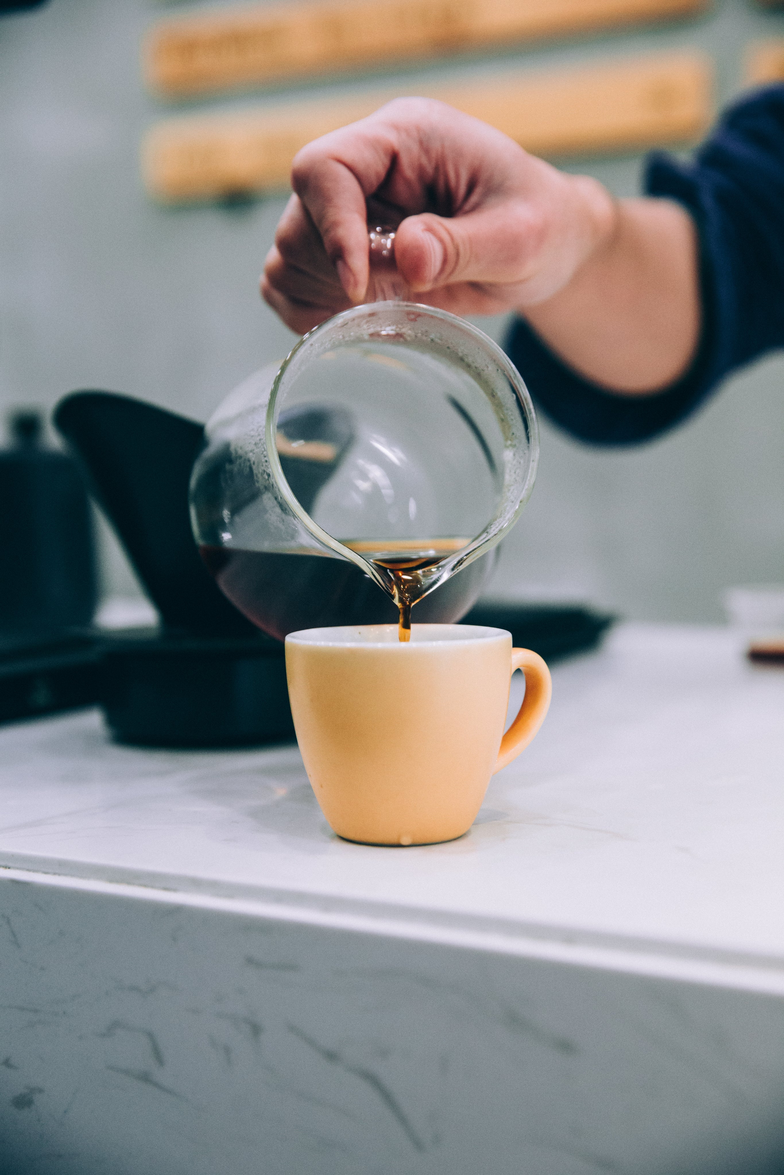 Glaskaraffe und Keramiktasse in gelb, Kaffe wird eingeschenkt, auf Marmortheke.