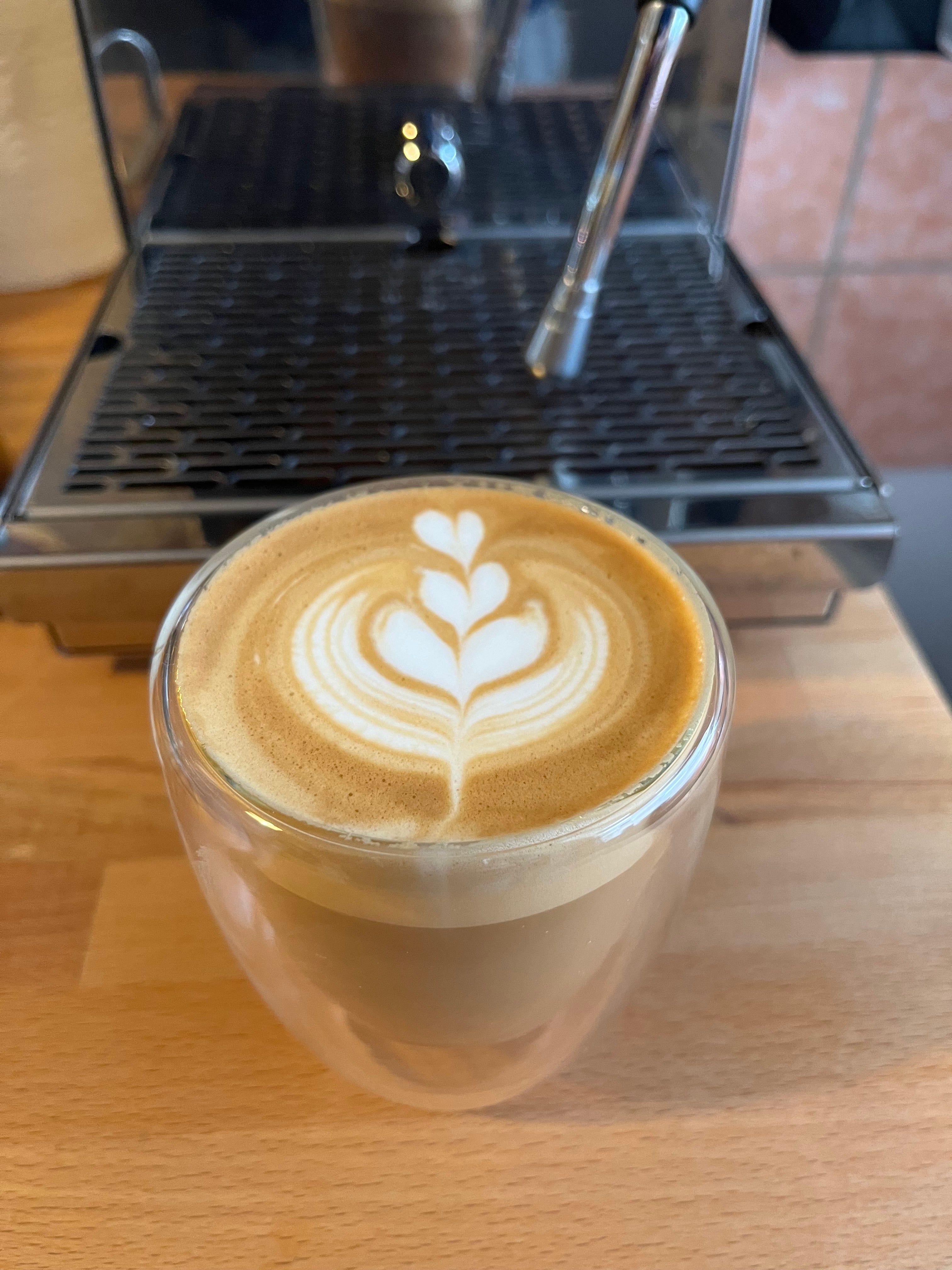 Latteart Tulpe in Glas, vor silberner Espressomaschine.