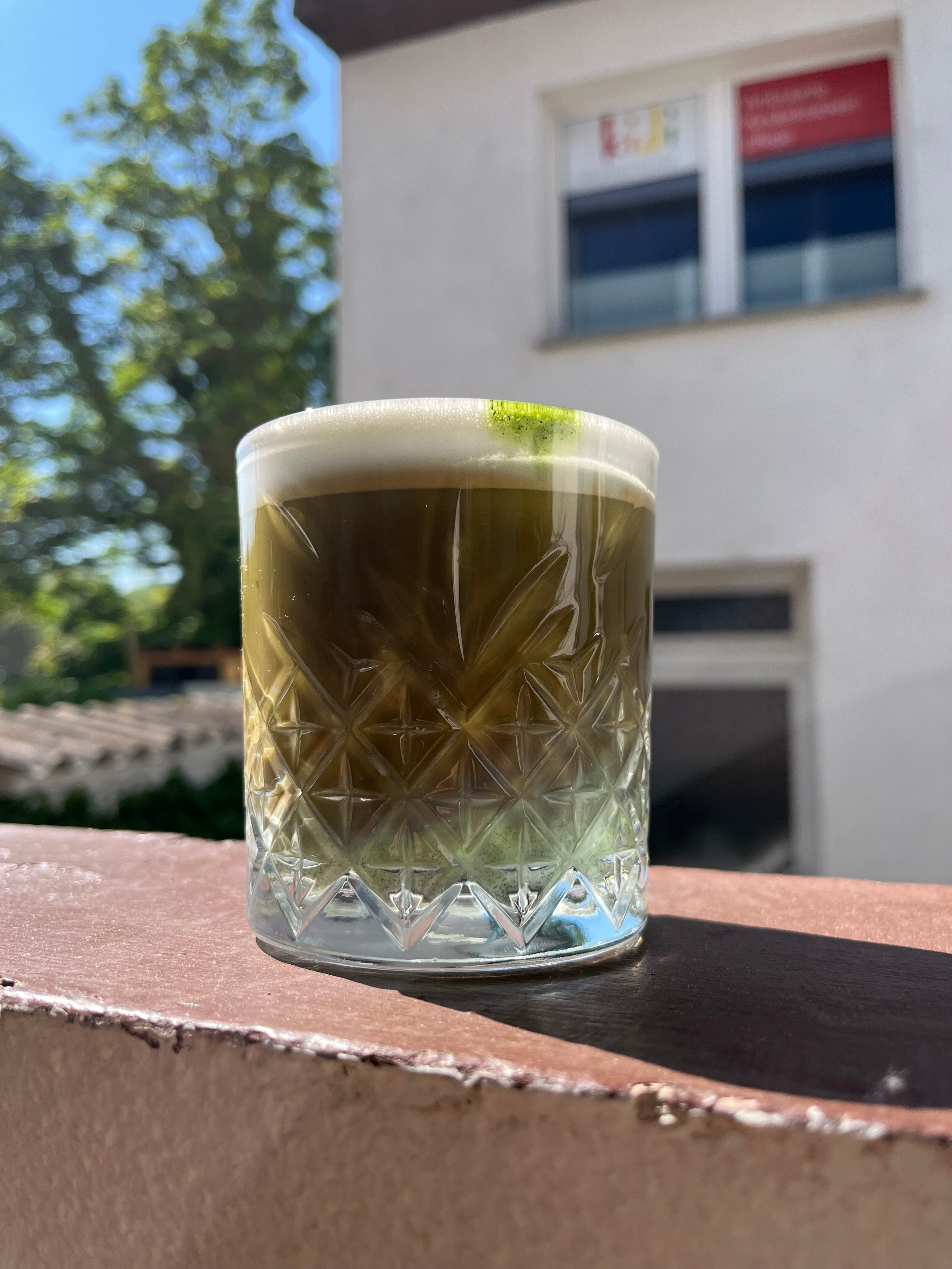 Matchalatte mit Espresso in Cocktailglas auf Balkonballustrade.