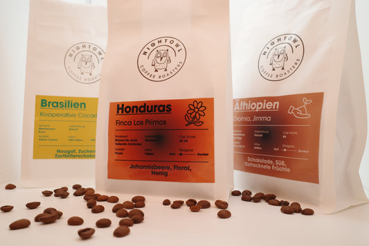 3 Packungen Kaffee mit Bohnen als Dekoration im Vordergrund.