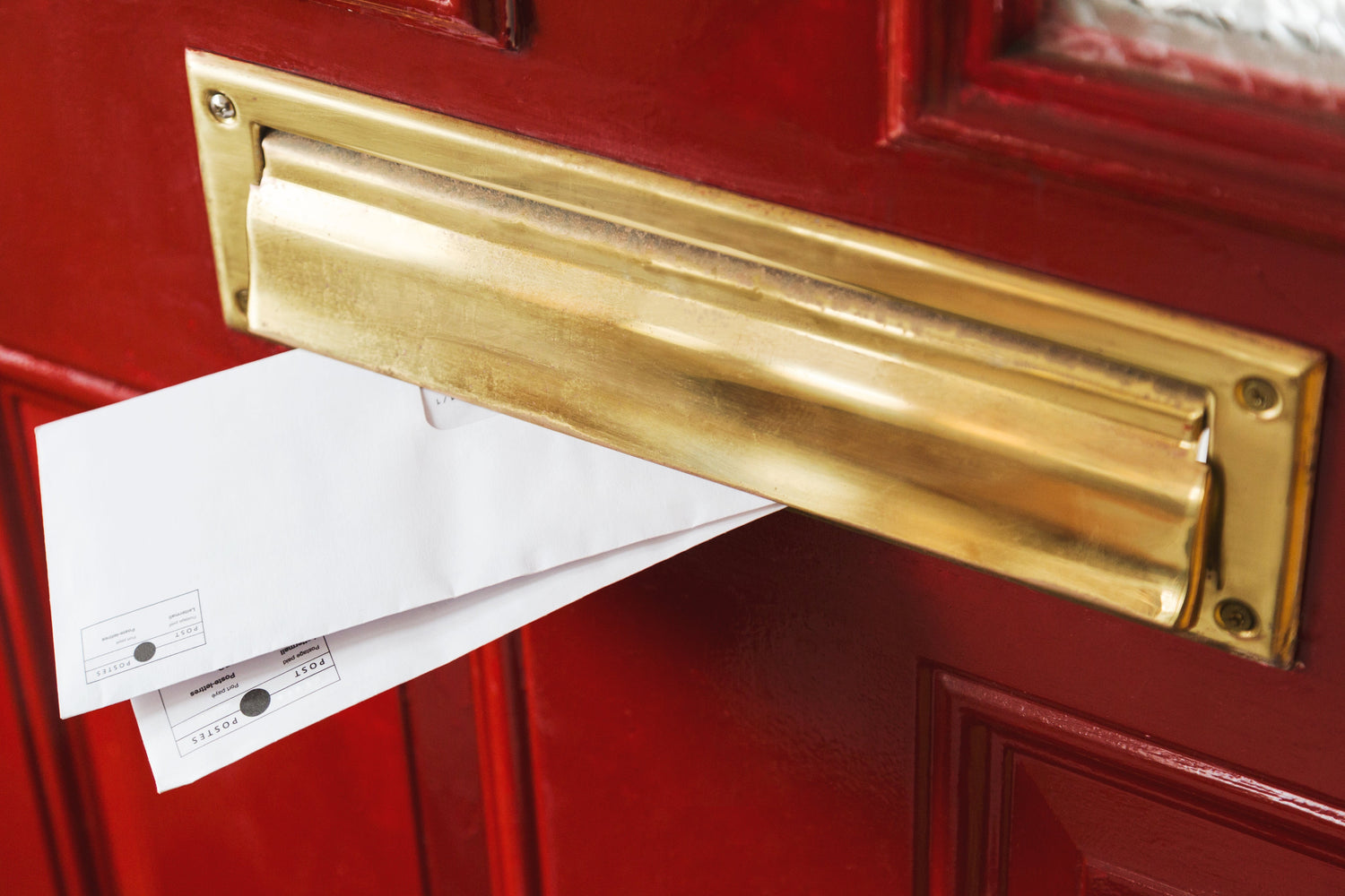 Rote Tür, goldener Briefkasten, zwei Briefe schauen heraus.